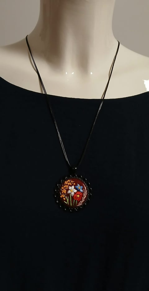 Mannequin wearing a black off-shoulder top with a long chain necklace featuring a decorative floral pendant with red and orange flowers