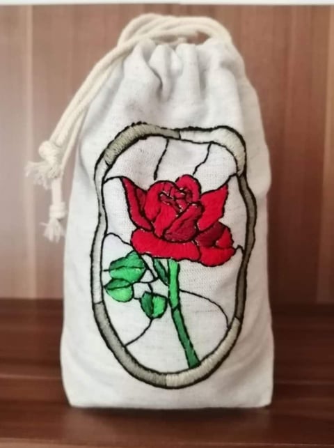 White cotton drawstring pouch with embroidered red rose and green stem in oval frame design