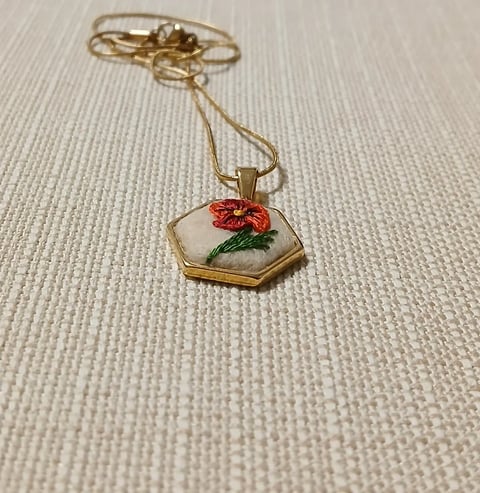 Gold hexagon pendant necklace with red flower and green leaf on cream textured background