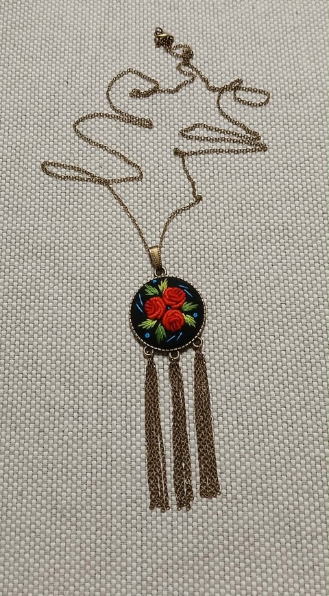 Vintage gold chain necklace with red roses pendant and tassel fringe displayed on cream textured fabric
