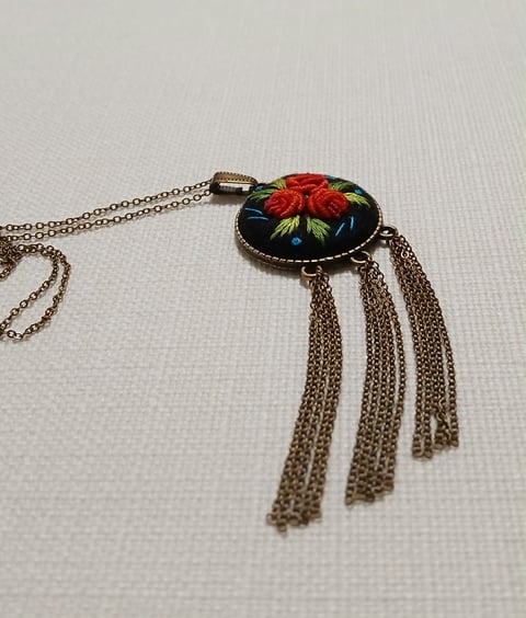 Ornate pendant necklace with embroidered red floral design on black oval setting and dangling chain tassels