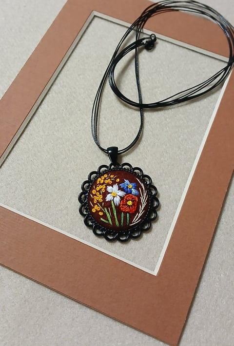 Handmade pendant necklace featuring colorful embroidered flowers in a black scalloped frame with cord string