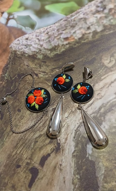 Three handmade jewelry pieces with black enamel faces decorated with orange flowers displayed on a textured wooden surface