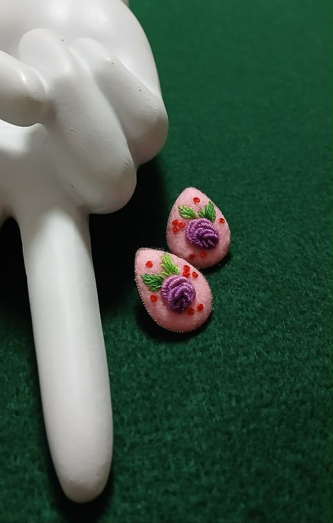 Two small decorative eggs with purple and pink floral embroidery designs next to a white ceramic figurine on green felt