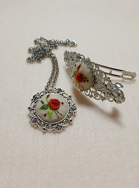 Vintage-style jewelry set with ornate silver filigree chain and two rose-decorated pendants on white surface