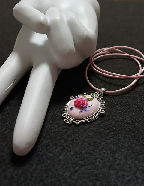 White ceramic hand figurine next to a rose pendant necklace with pink leather cord on dark background
