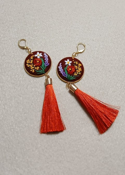 Two decorative enamel keychain charms with floral designs and red silk tassels hanging from gold clasps.