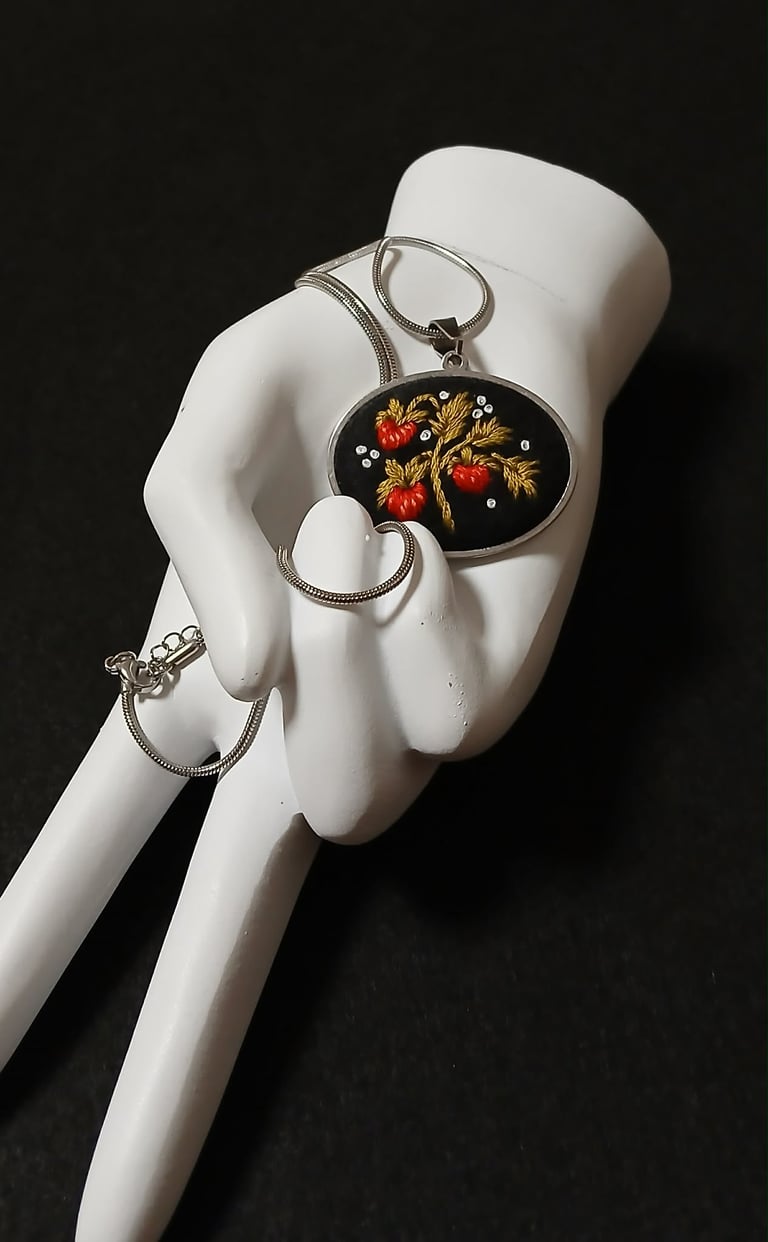 White mannequin hand holding decorative pendant bracelet set with oval fruit motif cameo against dark background