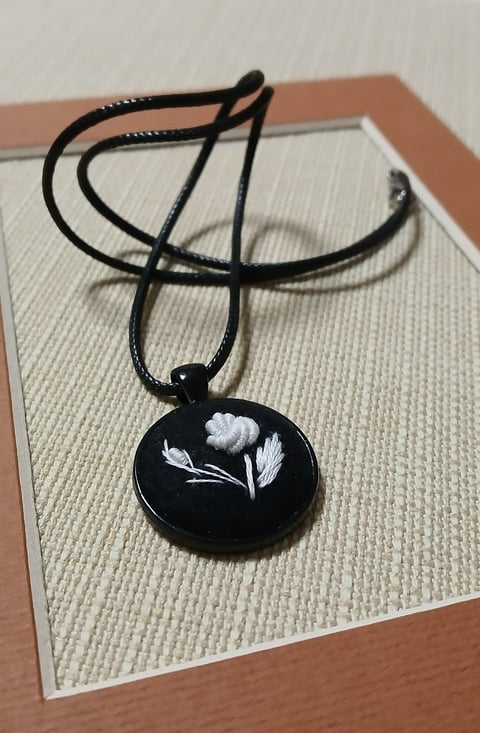 Black pendant necklace with white flower design on textured cream and tan display board
