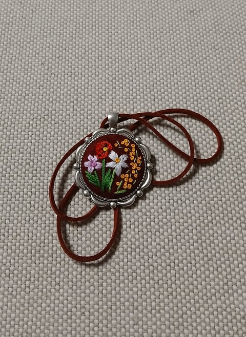 Decorative bolo tie with ornate silver pendant featuring colorful embroidered flowers on brown leather cord