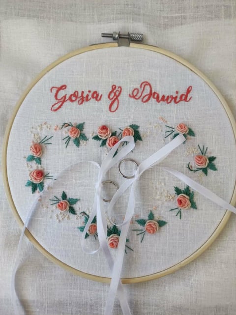 Embroidery hoop with Gosia & David text, floral design with roses, and white ribbon bow with wedding rings attached