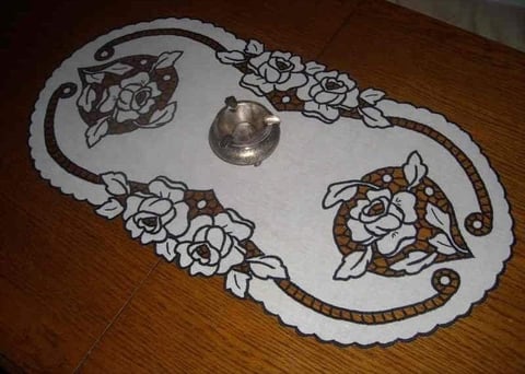 White lace doily with brown floral embroidery and ornate borders on wooden surface