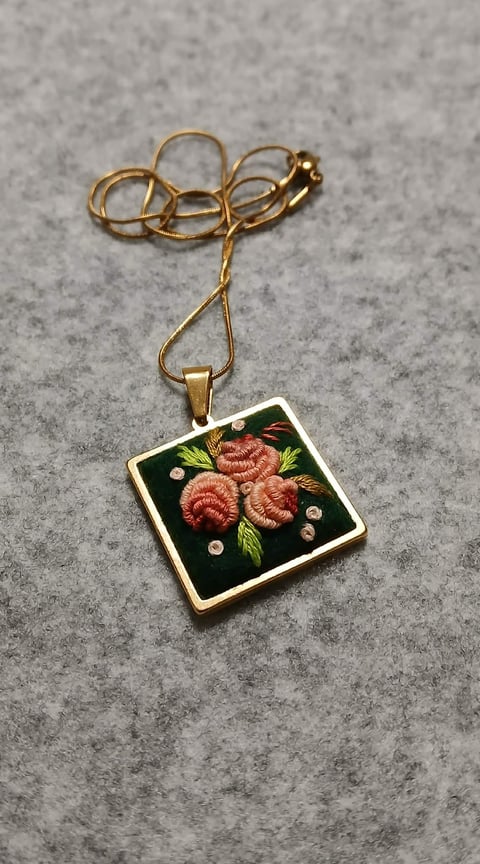 Gold necklace with embroidered square pendant featuring red raspberries and green leaves on dark background