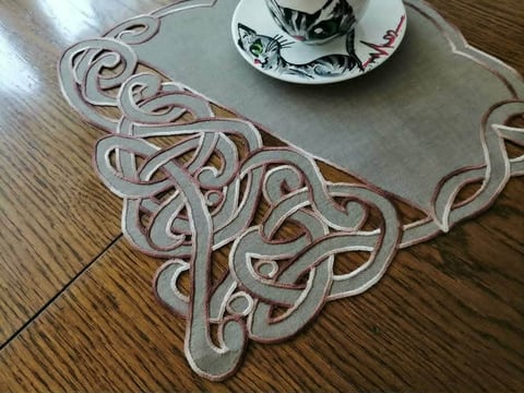 Decorative Celtic-patterned placemat with ornate knotwork design in cream and burgundy, topped with a decorative teacup on wooden surface