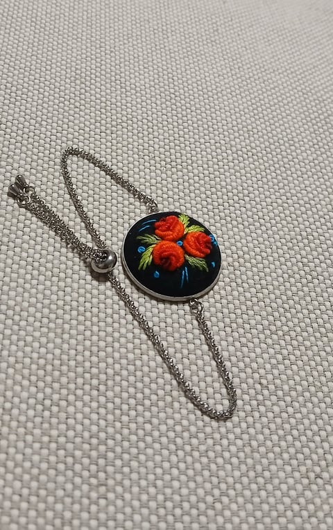 Silver chain necklace with circular pendant featuring red flowers on black background