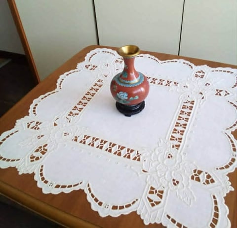 Decorative red and blue ceramic vase with brass spoon on white lace doily placed on wooden table