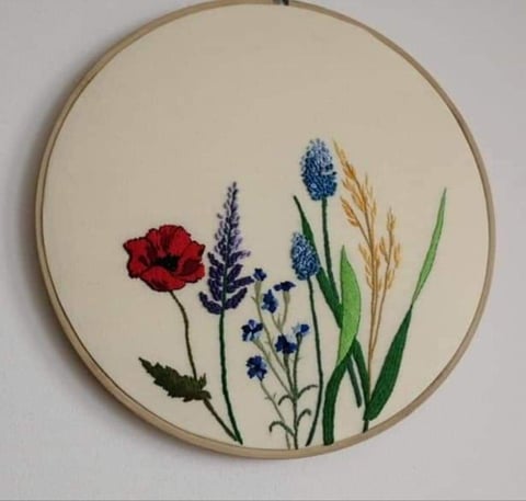 Embroidered flowers in hoop: red poppy, blue veronica, lavender, wheat, and green stems on cream fabric