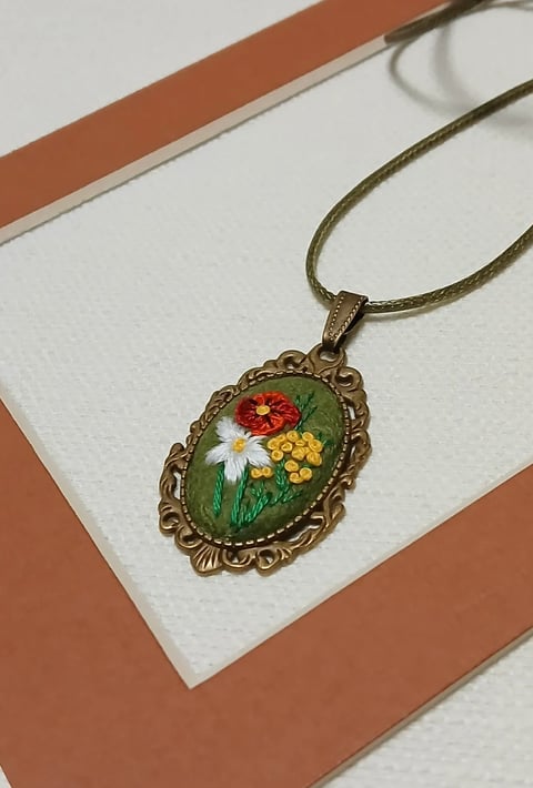 Vintage-style floral pendant necklace with ornate brass frame featuring red and yellow flowers on green background