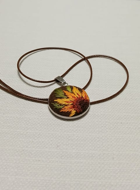 Pendant necklace with brown cord featuring a circular resin charm with dried sunflower pressed inside