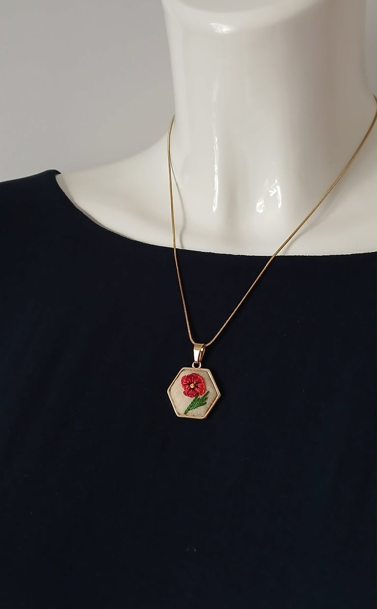 Gold chain necklace with hexagonal pendant featuring red flower design, displayed on mannequin wearing black top