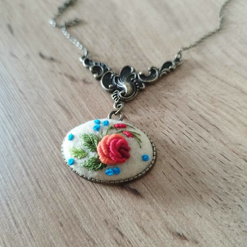 Handmade pendant necklace with ornate silver chain and decorative oval charm featuring embroidered red rose and blue flowers on cream fabric