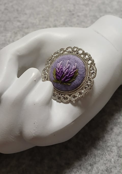 Silver ornate ring with purple pressed flower resin stone displayed on white ceramic hand form