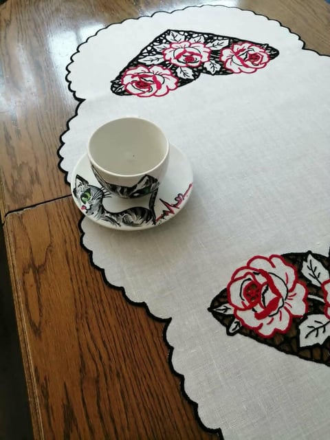 Teacup and saucer on white scalloped tablecloth with floral embroidery featuring pink and red roses