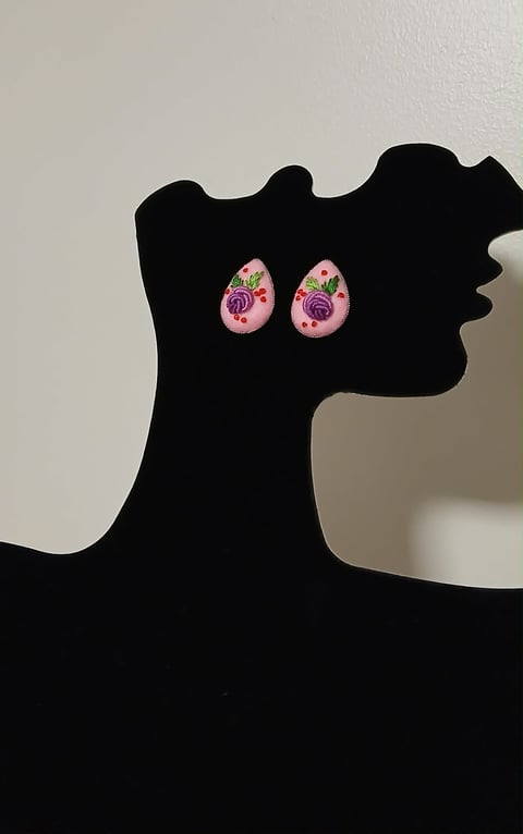 Black silhouette of a womans profile wearing pink floral teardrop-shaped earrings against a light background