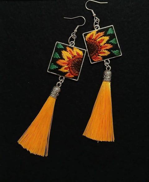 Pair of ornate earrings with sunflower designs and yellow tassel pendants on black background