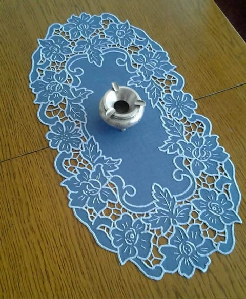 Blue lace doily with ornate floral pattern and silver candle holder placed in the center on wooden floor