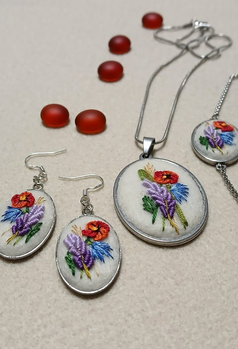 Embroidered floral jewelry set featuring a pendant necklace and matching earrings with red and blue flowers on white background with red beads