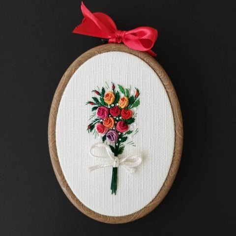 Embroidered floral bouquet in wooden oval frame with red ribbon bow on dark background