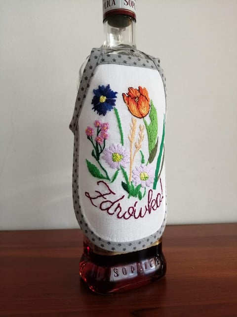 Clear glass vodka bottle with embroidered fabric wrap featuring colorful flowers and Zubrowka branding