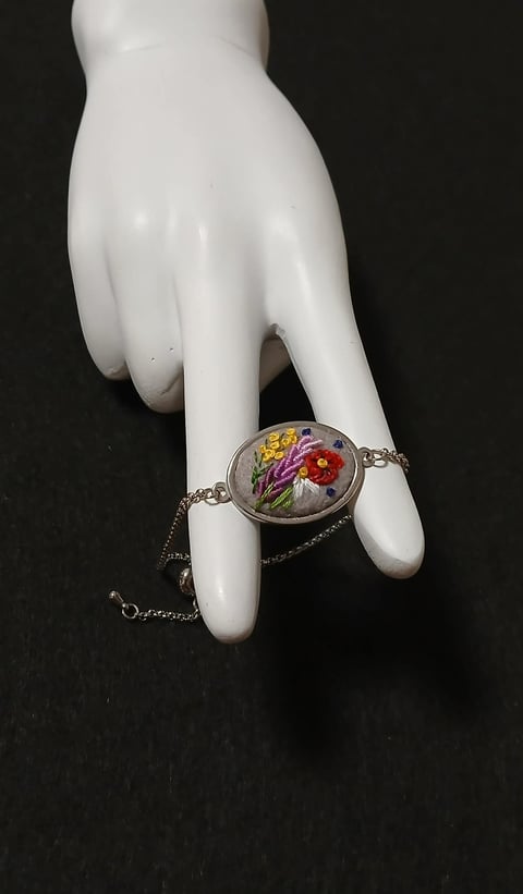 White ceramic hand wearing a floral bracelet with colorful embroidered flowers on dark background