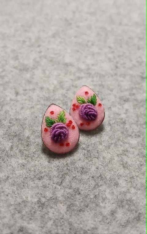 Two pink resin earrings with purple flowers, red berries, and green leaves on gray textured background