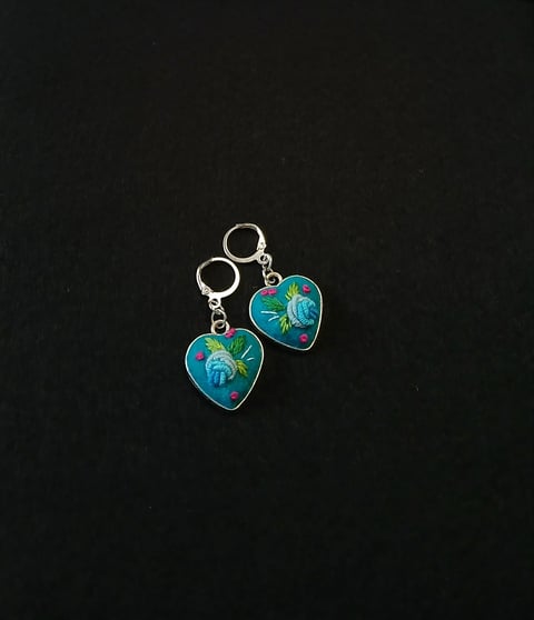Pair of turquoise and gold heart-shaped dangle earrings with floral design on black background