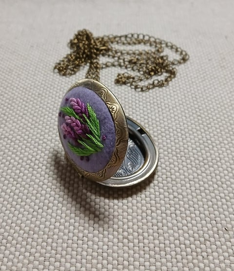 Oval locket necklace with purple resin pendant containing dried purple flowers and green foliage, on bronze and silver chain