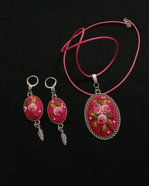 Silver jewelry set with pink roses on dark background: matching earrings and pendant necklace with decorative charms