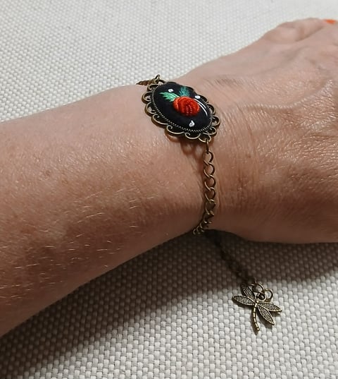 Ornate silver bracelet with red and green beetle cameo pendant worn on wrist, displayed on light background