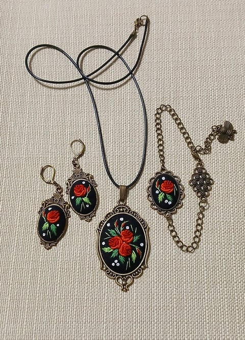 Vintage-style jewelry set featuring rose-decorated cameo pendant and matching earrings on metal chains against cream textured background