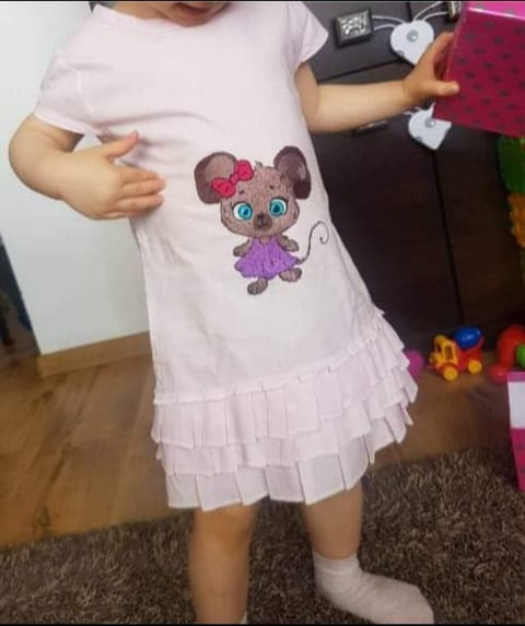 Child wearing a light pink t-shirt dress with a cute cartoon cat graphic featuring pink bows and blue eyes, styled with a ruffled hem.