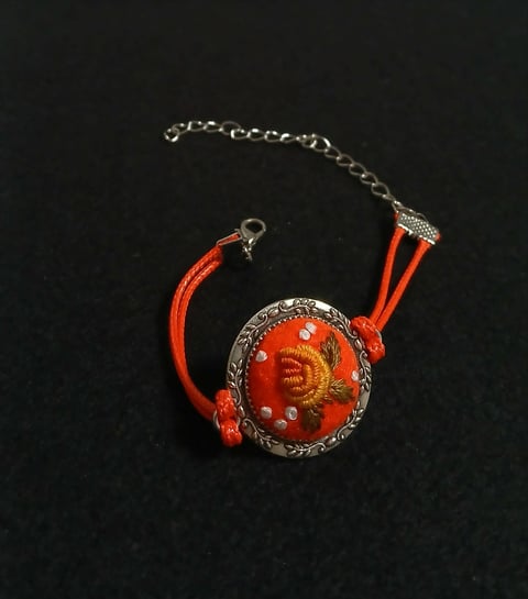 Ornate red and gold pendant bracelet with decorative metal filigree, red fabric straps, and silver chain on black background