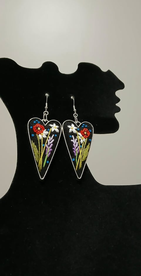Pair of heart-shaped resin earrings featuring dried flowers and plants on black silhouette bust display