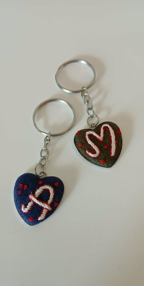 Two decorative heart-shaped keychains with candy cane designs attached to silver metal key rings on a light background.