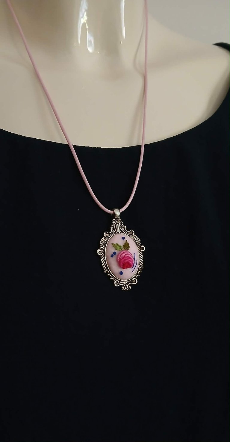 Woman wearing ornate silver pendant necklace with pink cord, featuring floral design with pink rose on cream background