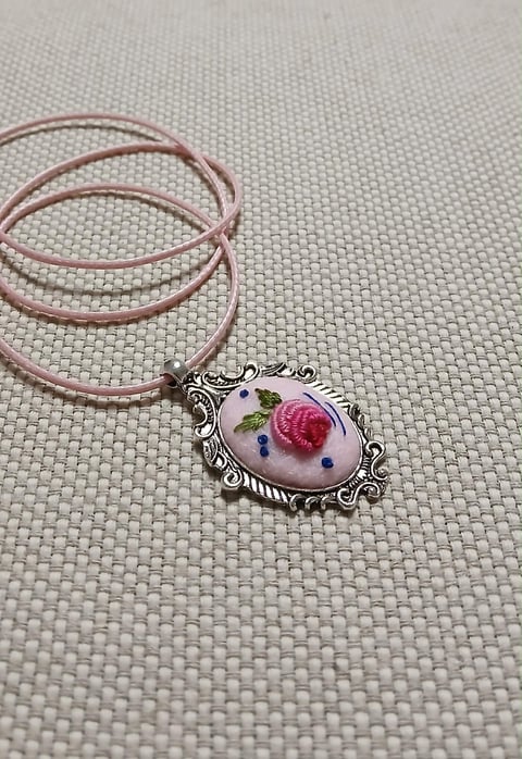 Ornate silver pendant with pressed flowers on pink cord necklace against textured white background