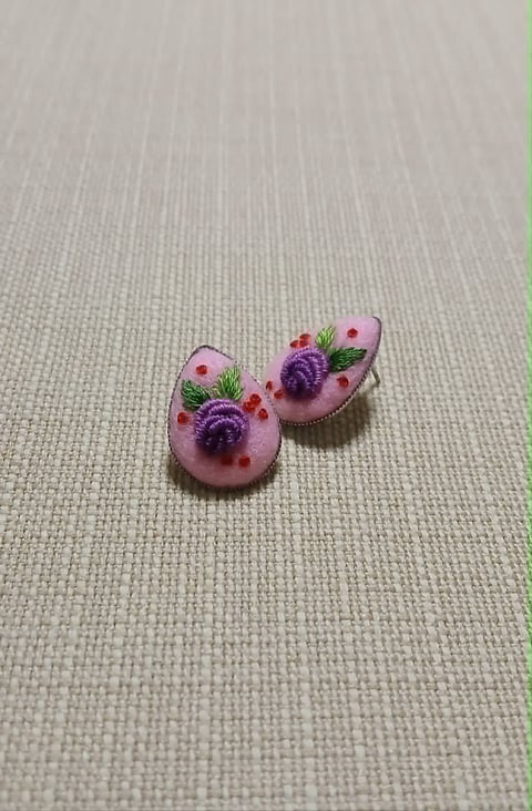 Pair of handmade earrings with pink resin domes featuring tiny purple flowers and green leaves on beige linen background