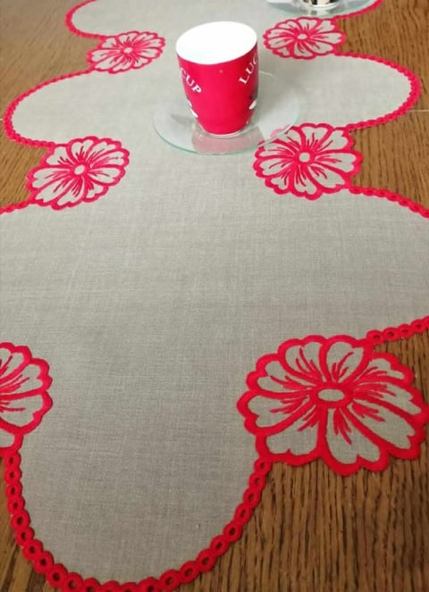 Cream linen placemat with pink embroidered flowers and scalloped edges, topped with a pink mug on wooden table