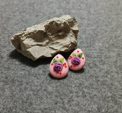 Pair of pink polymer clay earrings with purple flower designs next to a cream-colored rock on gray surface