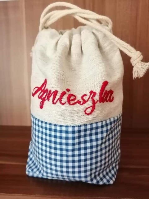 Cream canvas drawstring bag with red Abuela text and blue gingham fabric base on wooden background